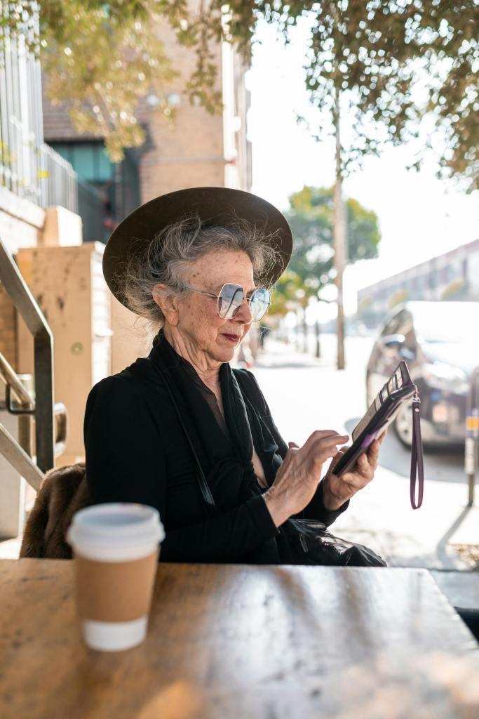 An poshly dressed elder lady sitting at an outdoor cafe and testing on her phone.